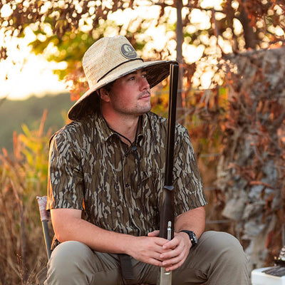 man sitting in chair wearing a straw hat in mossy oak original bottomland